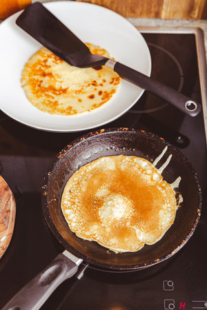 Making thin pancakes on frying pan in kitchen, with cooking dough for crepes and pancakes.の写真素材