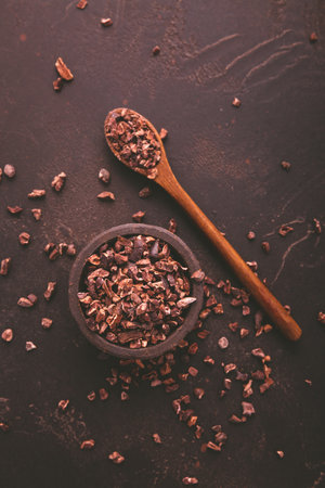 Organic cocoa nibs and cocoa beans in a bowl on brown backgroundの写真素材