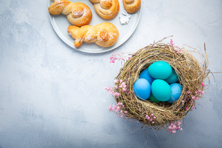 Easter eggs in nest with sweet buns made from yeast dough in a shape of Easter bunnyの写真素材