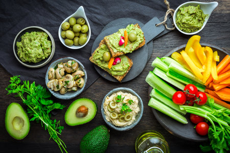 Vegan raw food snacks with fresh juicy vegetables, avocado dip, humus and marinated mushroomsの写真素材