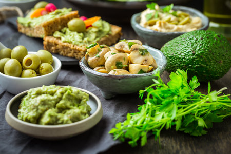 Vegan raw food snacks with fresh juicy vegetables, avocado dip, humus and marinated mushroomsの写真素材