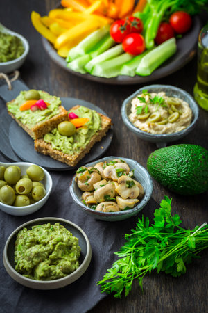 Vegan raw food snacks with fresh juicy vegetables, avocado dip, humus and marinated mushroomsの写真素材