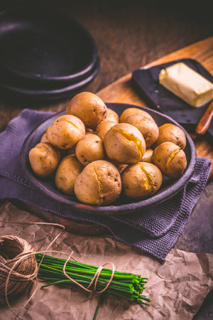 Boiled young potatoes with butter and chives on cutting boardの写真素材