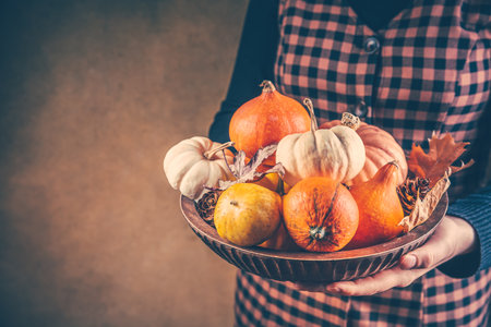 Thanksgiving and Halloween concept. Woman holding bowl decorated with pumpkinsの写真素材