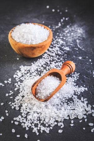 Pure natural sea salt in wooden bowl and wooden spoon on black backgroundの写真素材