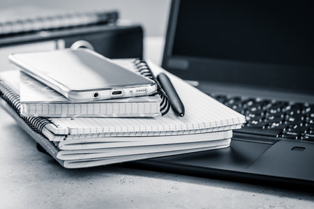 Office table - stack of notebooks, cellphone with laptopの写真素材