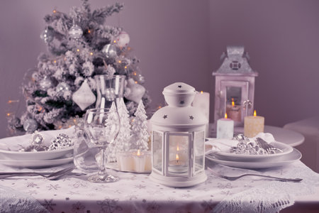 Festive  Christmas table place setting with silverware, candles and decorated Christmas treeの写真素材