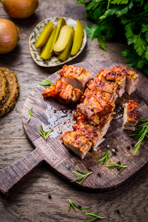 Roasted pork belly with crust,  pickles and bread on cutting boardの写真素材