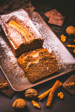 Homemade vegan banana bread or cake with nuts, chocolate and cinnamon on brown backgroundの写真素材