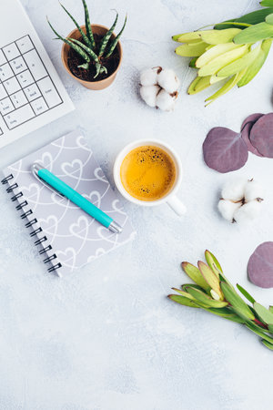 Workplace with cup of coffee, empty notebook, keyboard, supplies and flowers in bright toneの写真素材
