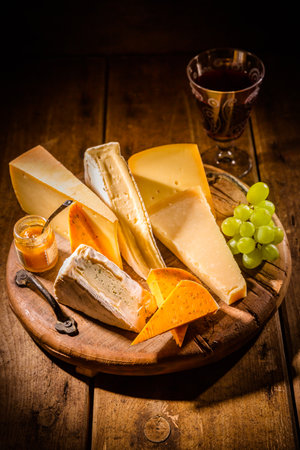Cheese platter, assortment of different cheeses with glass of red wine, grapes on wooden tableの写真素材