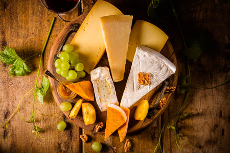 Cheese platter, assortment of different cheeses with glass of red wine, grapes on wooden tableの写真素材