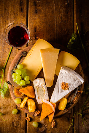 Cheese platter, assortment of different cheeses with glass of red wine, grapes on wooden tableの写真素材