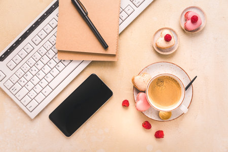 Feminine business workplace with keyboard, writing supplies, cup of coffee and small macarons in bright toneの写真素材