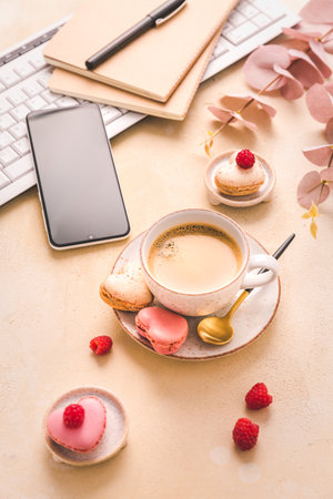 Feminine business workplace with keyboard, writing supplies, cup of coffee and small macarons in bright toneの写真素材