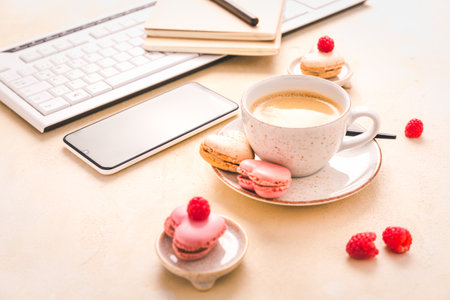 Feminine business workplace with keyboard, writing supplies, cup of coffee and small macarons in bright toneの写真素材