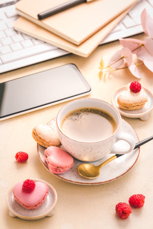Feminine business workplace with keyboard, writing supplies, cup of coffee and small macarons in bright toneの写真素材