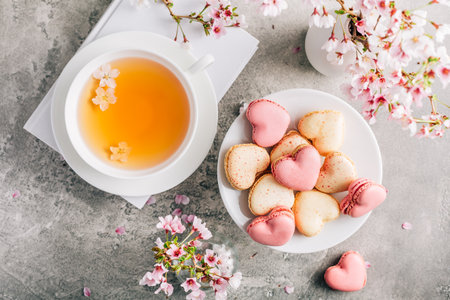Macarons or French macaroons in heart shapes with tea with cherry blossom petals for Mothers Dayの写真素材