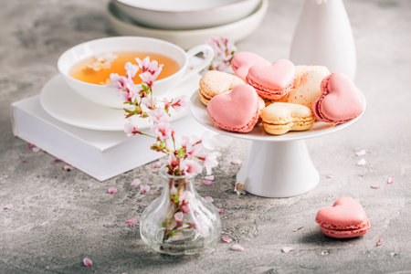 Macarons or French macaroons in heart shapes with tea with cherry blossom petals for Mothers Dayの写真素材