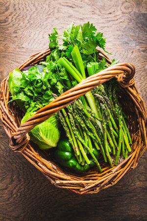 Fresh green vegetables and herbs in wicker basket, asparagus, lettuce, zucchini with parsley and cilantro  on wooden tableの写真素材