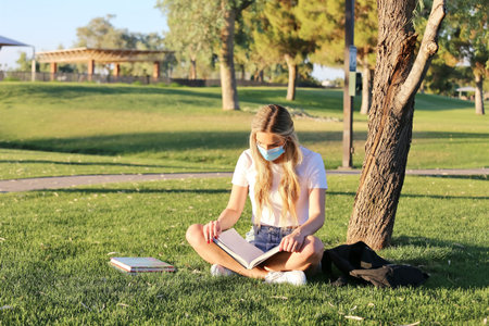 A student wearing a face mask studying outside while social distancing