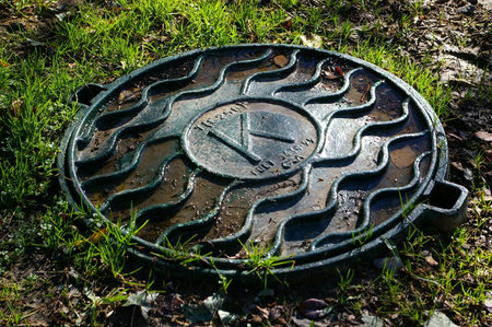 Old sewer manhole cover with grass and brown leavesの写真素材