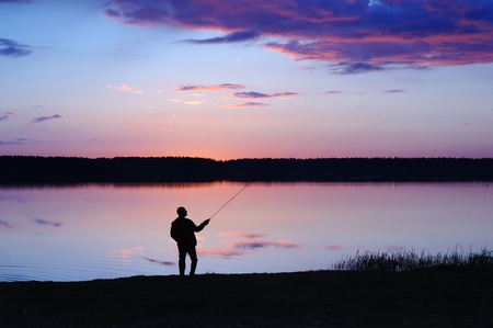 Silhouette of the fisher on a background of an evening dawnの写真素材