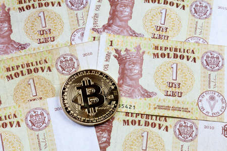 Close-up on a golden Bitcoin coin on top of a stack of Moldovan leu banknotes.の写真素材