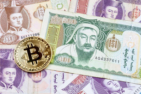 Close-up on a golden Bitcoin coin on top of a stack of Mongolian TÃ¶grÃ¶g banknotes.の写真素材