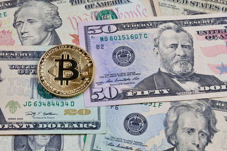 Close-up on a golden bitcoin coin on top of a stack of us dollars.の写真素材