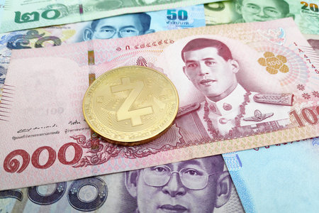 Close-up on a golden Zcash coin on top of a stack of Thai Baht banknotes.