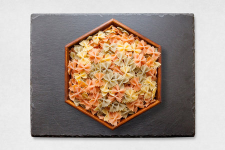 Slate tray on a white surface with on its middle, an hexagonal wooden dish with colorful bow tie...