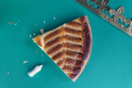 A piece of Northern French style galette des rois with the fÃ¨ve and the crown on a green...