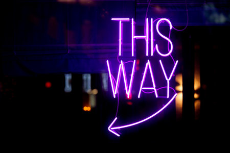Purple neon light inside a restaurant stating: "This way" above an arrow pointing left.の写真素材