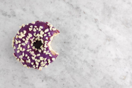 Donut with purple icing topped with small white chocolate crumb with one bite missing.の写真素材