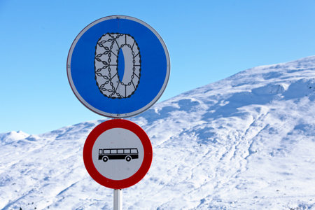 A snow chains required sign above a Prohibition of buses sign in front of a snow-capped mountain in the Pyrenees.の写真素材