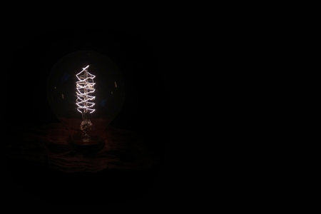 Close-up on a retro style light bulb screwed on a piece of wood isolated on black background.の写真素材