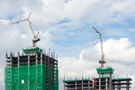 Two cranes each on the top of a skyscraper in construction.の写真素材