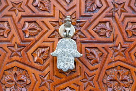 Close-up on a door knocker shaped into a Hamsa (Fatima's hand) on an old carved wooden door in the...