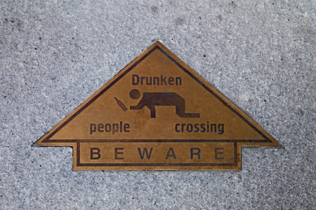 Brass arrow on a stone doorstep showing a drunk man with written the message drunken people crossing...