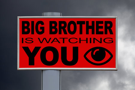 Close-up on a red billboard against a cloudy sky with the message "Big Brother is watching you" written in the middle next to an eye icon.の写真素材