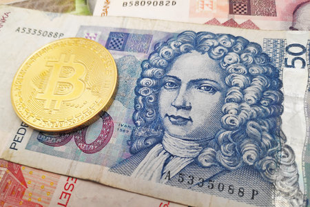 Close-up on a golden Bitcoin coin on top of a stack of Croatian Kuna banknotes.