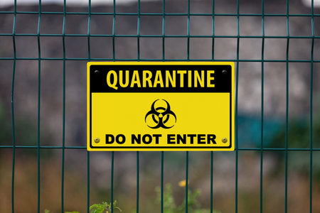 Black and yellow warning sign on a fence displaying a biohazard symbol and the message in Quarantine...