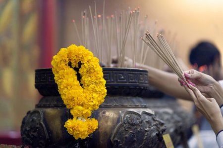 Prayers burning incense sticks and offering garland of flowers at Wat Hua Lamphong in Bangkok.の写真素材