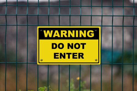 Black and Yellow warning sign attached on a fence. The sign stating âWarning - Do not enterâ.の写真素材