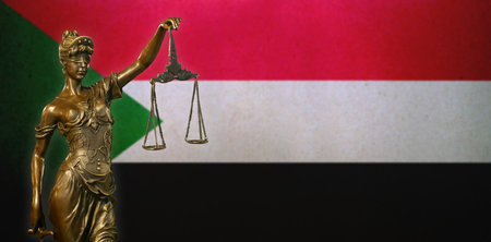 Close-up of a small bronze statuette of Lady Justice before a flag of Sudan.の写真素材