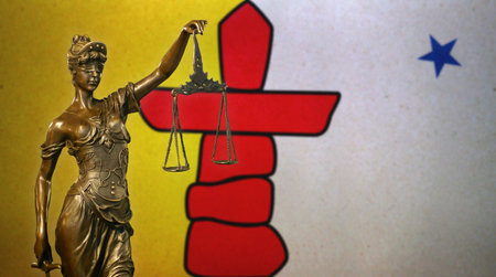 Close-up of a small bronze statuette of Lady Justice before a flag of Nunavut (Canada).の写真素材