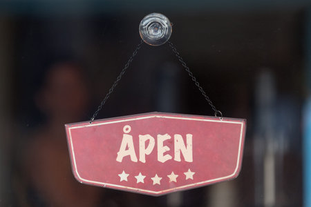 Old fashioned sign in the window of a shop saying in Norwegian Ã…pen, meaning in English Open.