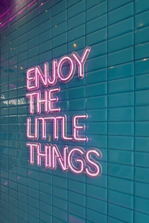 Pink neon light on a green tile wall saying: Enjoy the little things.の写真素材
