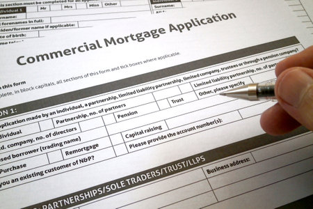 A ballpoint pen between the fingers of a man filling a commercial mortgage application form.の写真素材